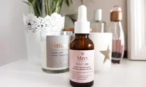 Brązowa buteleczka serum Miya Beauty.lab z pipetką na jasnoróżowej etykiecie, na tle świecy i roślin.