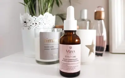 Brązowa buteleczka serum Miya Beauty.lab z pipetką na jasnoróżowej etykiecie, na tle świecy i roślin.
